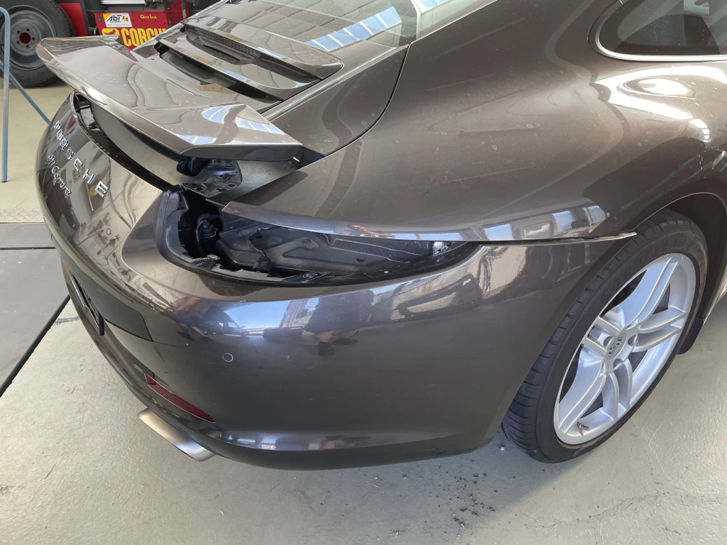 Die RÜckseite eines grauen Porsches mit Schaden am Heck, die rechte Rücklampe fehlt. Nahaufnahme.
