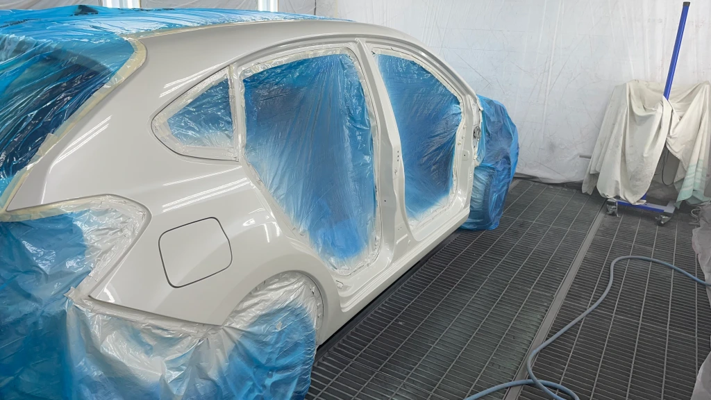 Ein Auto dessen Fenster und Türen entfernt worden sind. Dort befindet sich jetzt blaue Plastikfolie. Der Rest wird frisch angesprüht bzw. lackiert.