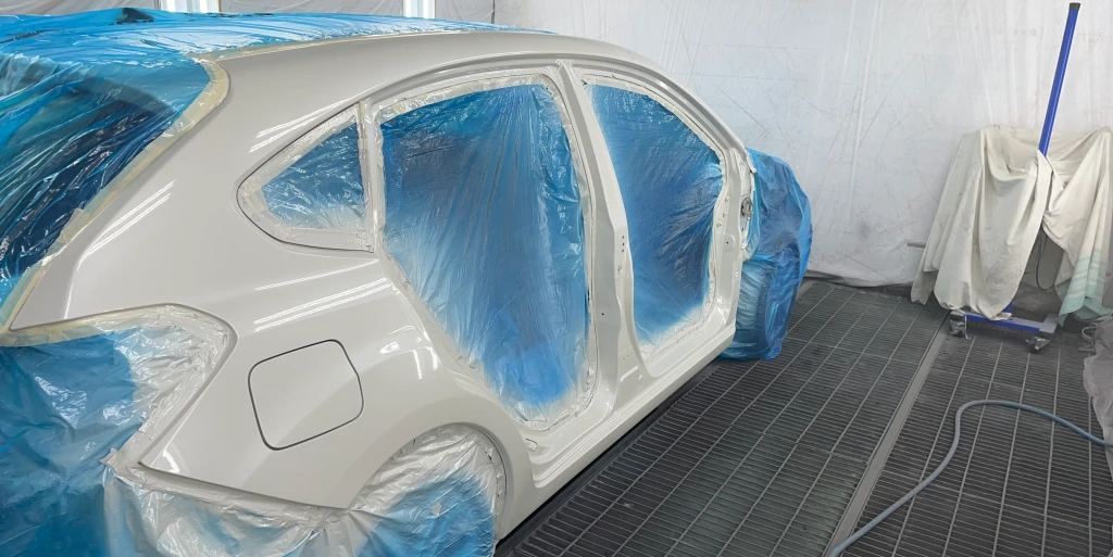 Ein Auto dessen Fenster und Türen entfernt worden sind. Dort befindet sich jetzt blaue Plastikfolie. Der Rest wird frisch angesprüht bzw. lackiert.